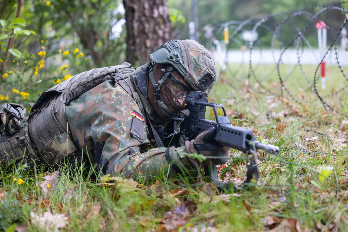 Bundeswehr-Rekruten beobachten liegend im Gras das Gelände mit Ferngläsern